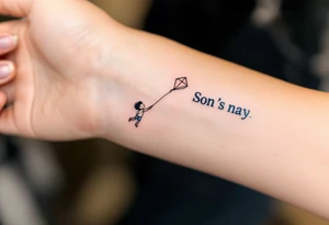 A line-art drawing of a child flying a kite, with the kite string forming the son’s name in dark navy ink. tattoo idea