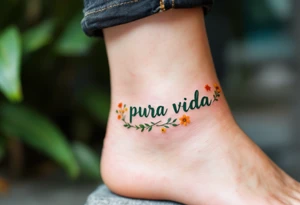 “Pura Vida” curving along the ankle, in dark green, surrounded by tiny wildflowers in orange and yellow. tattoo idea