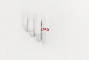 A tiny, delicate red band looped around the finger tattoo idea