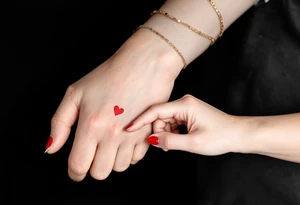 Thin black line tattoos of two hands making a pinky promise, with a tiny red heart between them.
Placement: Side of the index finger or wrist. tattoo idea