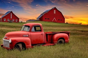 A broken down rustic red '53 5-window GMC long bed pickup parked at an angle in front of a red barn with the setting sun in the background. The setting sun is shaped like a sunflower. tattoo idea